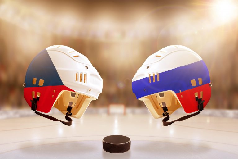 Low angle view of hockey helmets with Czech Republic and Russia flags painted and hockey puck on ice in brightly lit stadium background. Concept of in