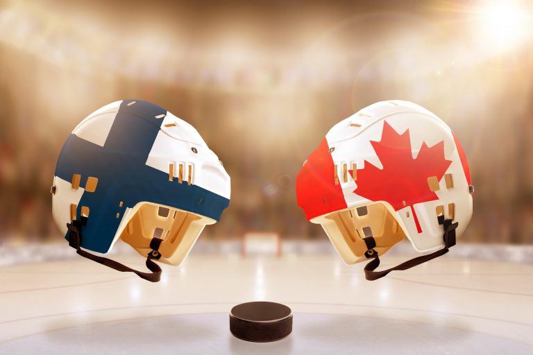 Low angle view of hockey helmets with Canada and Finland flags painted and hockey puck on ice in brightly lit stadium background. Concept of intense r