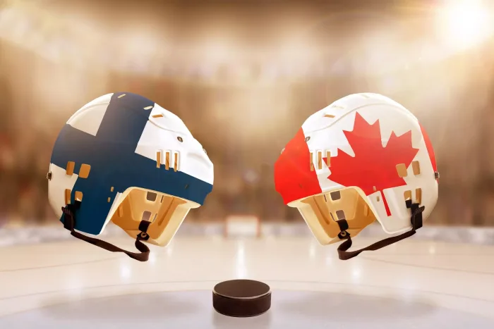 Low angle view of hockey helmets with Canada and Finland flags painted and hockey puck on ice in brightly lit stadium background. Concept of intense r Kanada – Finland, 1/6: Speltips & stream (Hockey VM)