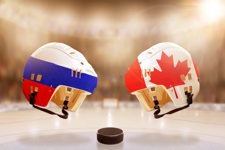 Low angle view of hockey helmets with Canada and Russia flags painted and hockey puck on ice in brightly lit stadium background. Concept of intense ri