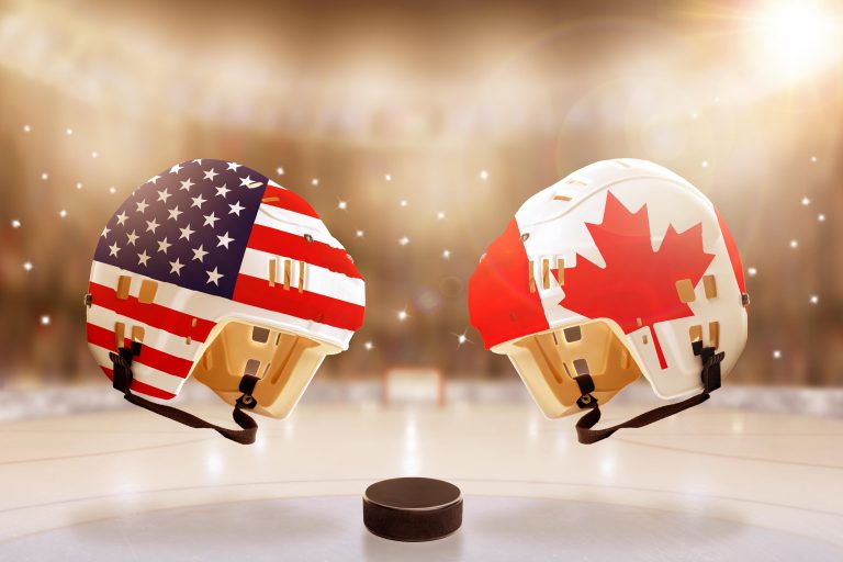 Low angle view of hockey helmets with Canada and USA flags painted and hockey puck on ice in brightly lit stadium background. Concept of intense rival